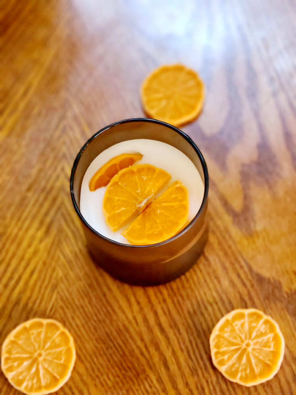 Joyful Spice candle with cinnamon orange clove scent and dried orange slices on wooden table.
